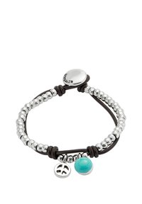 Pulsera de cuentas en tono plateado con un cordón de cuero negro, que presenta una cuenta turquesa y un charm de símbolo de la paz en plata. Cierre ajustable.