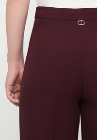 Burgundia püksid sujuva tekstuuriga, millel on vööklammer, ja kohandatud lõige, koos lihtsa valge toppiga.