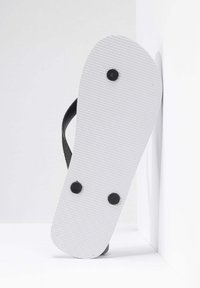 Sort flip-flop med en struktureret gummistrop og en hvid sål med et diamantmønster og fire sorte nitter.