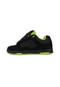Zapatilla de ante negro con un acento verde en el cuello, suela de goma y paneles texturizados en negro. Diseño con cordones y perfil bajo.