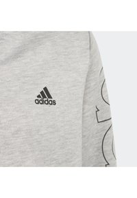 Szary sweter z czarnym logo Adidas na klatce piersiowej. Charakteryzuje się gładką teksturą i prostym wzornictwem, z subtelnym wzorem graficznym na rękawie.