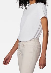 T-shirt blanc à manches courtes en tissu doux, associé à un jean beige clair ajusté. La tenue présente un design simple et une coupe décontractée.