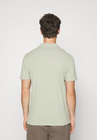 Lichtgroene polo met korte mouwen, een kraag en een rechte zoom. Zachte textuur en een ingetogen ontwerp zonder zichtbare patronen of accenten.
