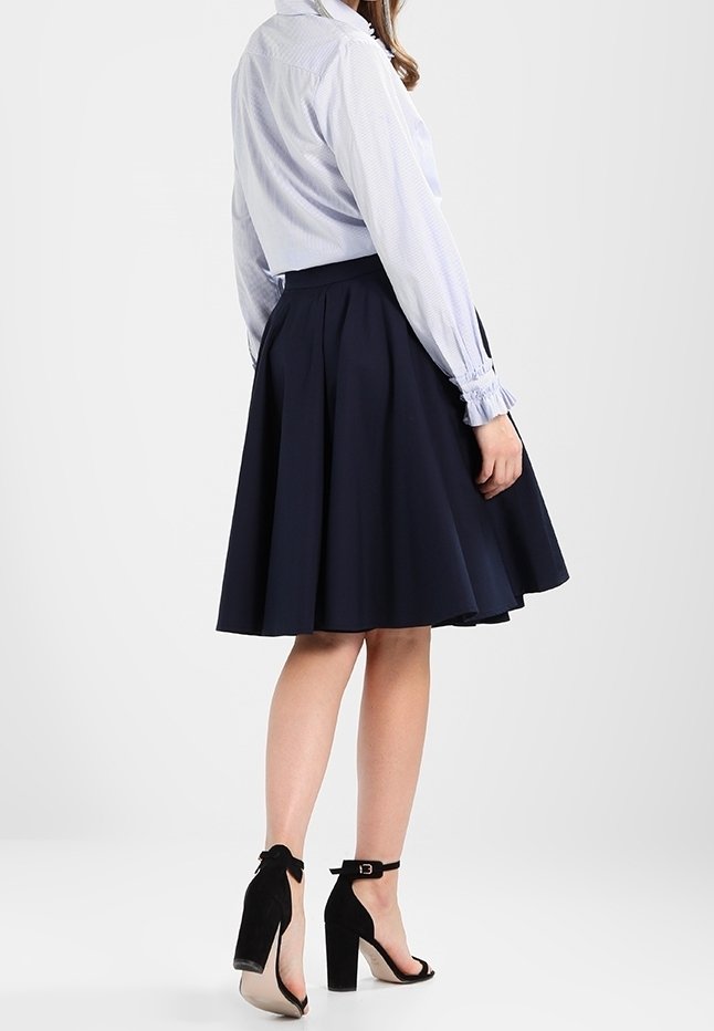 Chemise à rayures bleues et blanches à boutons, associée à une jupe patineuse navy foncé. Des sandales à talons noirs ajoutent du contraste. Textures lisses, design classique.