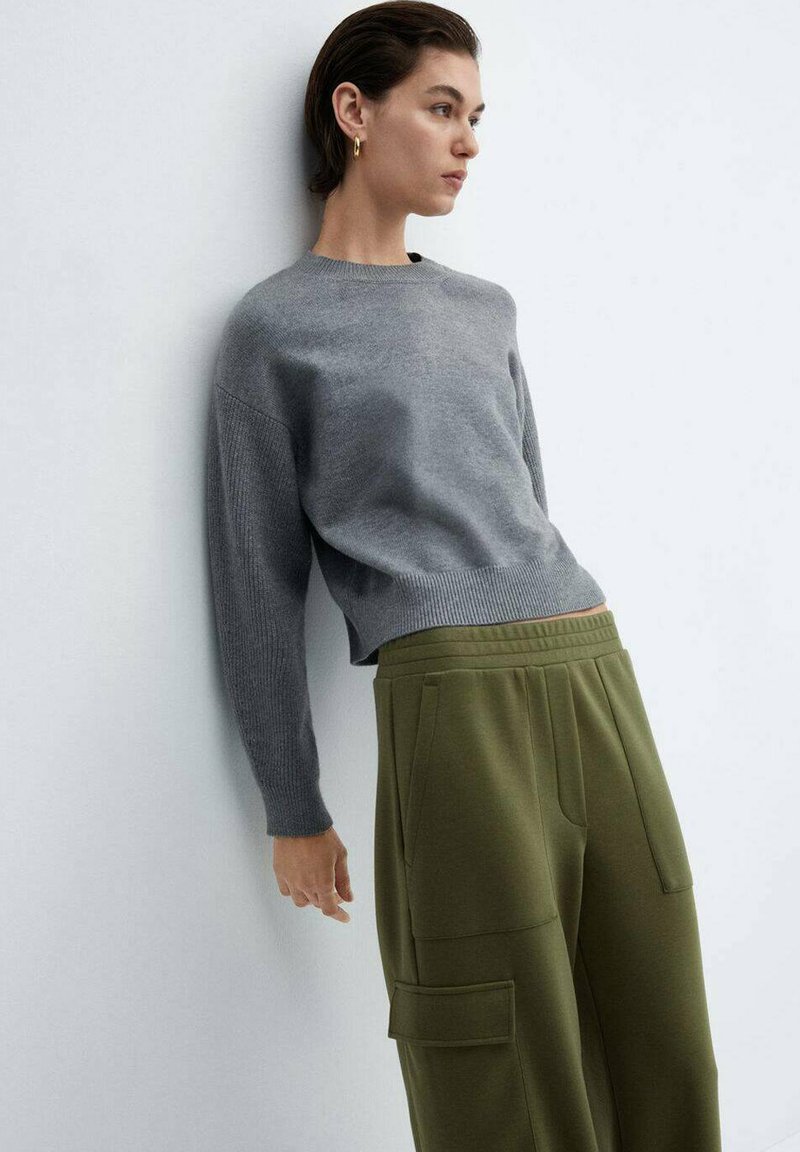 Suéter gris de punto con cuello redondo y mangas texturizadas, combinado con pantalones de chándal verde oliva que cuentan con bolsillos laterales y una cintura elástica.