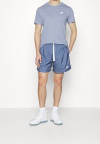 Herrarnas ljusblå Nike-t-shirt med en liten vit logotyp; blåa shorts med elastisk midja; vita skor med synlig luftkuddsdämpning.