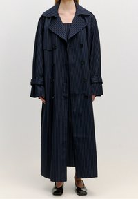 Marinblå randig trenchcoat med en stor krage, dubbelknäppta knappar och manschetter. Lång, rak design med en slät textur.