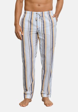 Man draagt lichtblauwe, gele, grijze en witte pyjamabroek met verticale strepen en trekkoord, staat blootsvoets met één hand in de zak.