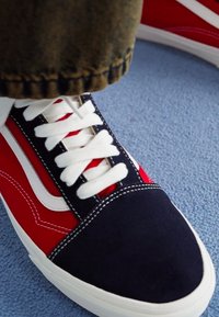 Low-top sneakers featuring a red and navy suede upper, white laces, contrasting stitching, and a white rubber sole. Textured fabric detail visible.