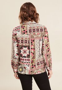 Camicia a maniche lunghe multicolore con un design a patchwork caratterizzato da motivi floreali e geometrici nei toni di marrone, rosa, bianco e nero.