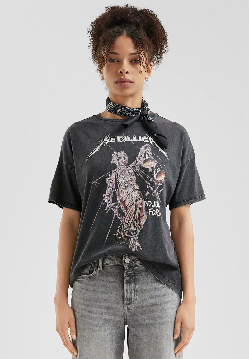 Zwarte graphic t-shirt met een versleten illustratie van een standbeeld dat schalen en een zwaard vasthoudt, met de tekst "Metallica" in een vet lettertype.