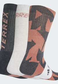 Tre paia di calzini: un paio nero con logo rosa, un paio bianco con una texture sottile e un paio grigio con un audace motivo geometrico in rosa.