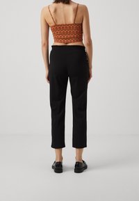 Pantalons noirs coupés associés à un crop top orange à motifs avec des fines bretelles. Texture lisse avec taille élastique ; chaussures noires simples.