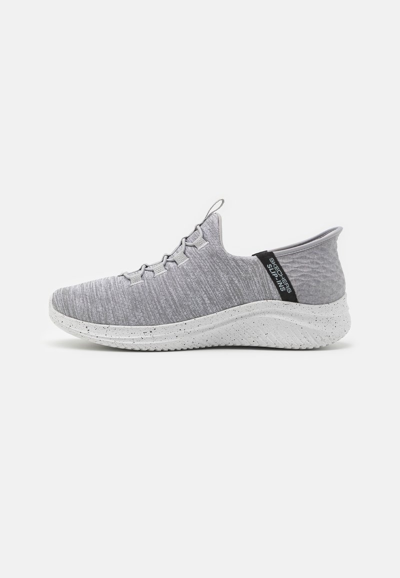 Baskets légères gris clair à enfiler avec tige en tissu texturé, semelle blanche tachetée, et languette de talon noire étiquetée "Skechers Slip-Ins."