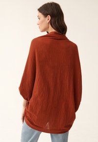 Maglione oversize leggero di colore ruggine con colletto drappeggiato e maniche a tre quarti. Il tessuto testurizzato crea un aspetto rilassato.