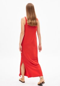 Rode maxi-jurk met tanktopbanden, gladde stof, een zijspli en een lichte curve aan de onderrand. Gekocht met lichtgekleurde sandalen.