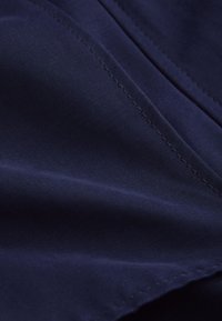 Nahaufnahme eines dunkelblauen Stoffs mit glatter Textur und detaillierter Naht entlang der Kante.