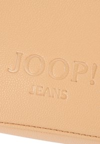 Bež usnjen denarnica z vtisnjenim napisom "JOOP! JEANS", gladko teksturo in podrobnostmi okoliščenega roba.