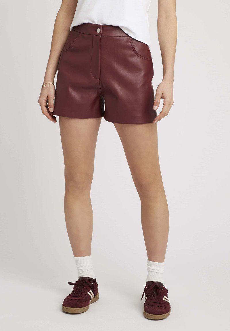 Shorts en simili cuir bordeaux avec une taille haute, des poches avant et une fermeture à un bouton. Fini avec une texture lisse et une coupe ajustée.