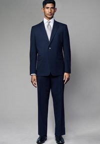 Námornícky prúžkovaný oblek s jedným gombíkom, skombinovaný s bielou košeľou a strieborn tie. Čierne formálne topánky dopĺňajú outfit.