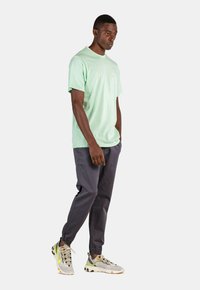 Camiseta de manga corta color verde menta, de corte suelto, combinada con pantalones jogger gris oscuro. Usada con zapatillas gris claro con acentos amarillos.