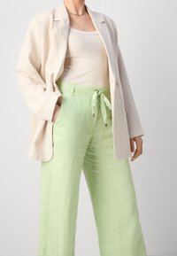 Krémový lněný blejzr přes bledě růžový top, v kombinaci se světle zelenými kalhotami s vysokým pasem a volným střihem, které mají stahovací pásky.