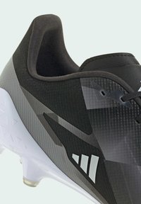 Crne i sive sportske cipele s teksturiranim gornjim dijelom, glatkim detaljima u akcentu i bijelom potplatu. Imaju podstavljenu obod i upečatljiv logo.