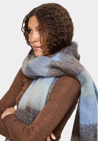 Strukturret uld tørklæde med vandrette striber i nuancer af blå, grå og brun, draperet om halsen og giver varme og dækning.