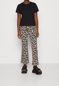 Svart bomullströja med korta ärmar, kombinerad med utsvängda leopardmönstrade byxor och tjocka svarta sandaler med texturerad sula.