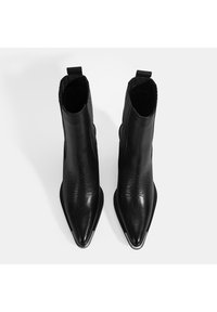 Bottines en cuir noir à bout pointu, avec des côtés nervurés et des détails en relief à l'avant. Comprend un tirant pour un enfilage facile.