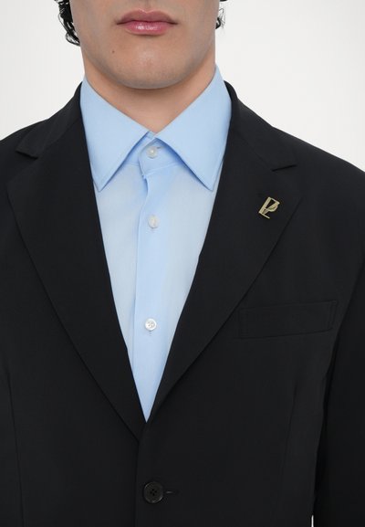 Schwarzer Blazer über einem hellblauen Hemd mit einem geknöpften Kragen. Mit einem goldenen Reverspin und einer Brusttasche ausgestattet. Glatte Textur, taillierte Passform.