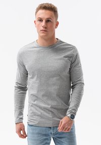 Graues Langarm-T-Shirt mit Rundhalsausschnitt, glatter Textur und taillierter Passform, kombiniert mit hellblauen Jeans und einer silbernen Uhr.