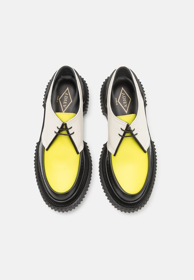 Chunky Schuhe mit einem weißen Obermaterial, einer leuchtend gelben Spitze und einer schwarzen Gummisohle mit Zickzackmustern. Ausgestattet mit schwarzen Schnürsenkeln und Markenlogo.