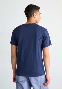 T-shirt en coton bleu marine à manches courtes, col rond et texture lisse, vu de dos. Design minimaliste, sans embellissements.