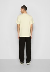 T-shirt amarelo claro de manga curta, combinado com calças de cargo pretas com bolsos laterais. O modelo é visto de costas, destacando o ajuste do conjunto.