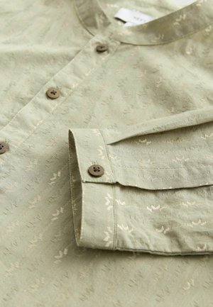 Lichtgroen overhemd met knopen, gemaakt van een gestructureerde stof met subtiele patronen, bruine knopen en een ronde kraag met een zachte afwerking.