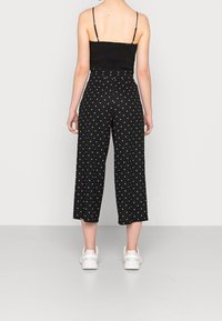 Svarta culotter med vita prickar, gjorda av mjukt tyg. Har en bred ben design och är kombinerade med vita sneakers.