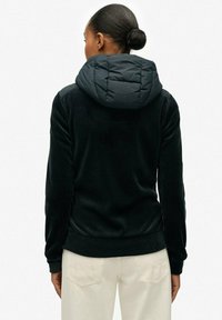 Sudadera negra con capucha gris acolchada y esponjosa; hecha de material suave; presenta un diseño ajustado y puños y dobladillo acanalados.