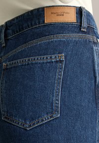 Ciemnoniebieskie dżinsy denim o dopasowanym kroju, z kontrastującymi pomarańczowymi przeszyciami i brązową skórzaną metką z napisem "Marc O'Polo DENIM".