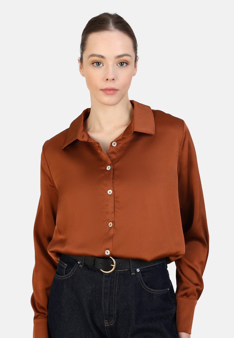 Braune Satinbluse mit Kragen und Knopfleiste, die eine glatte Textur aufweist. Getragen mit hochgeschnittenen dunkelblauen Jeans und einem schwarzen Gürtel.