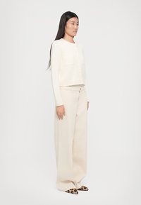 Elfenben cropped cardigan med to frontlommer og ribbestrikket kant, sammen med krèmefargede vide bukser og dyreprint spisse sko.