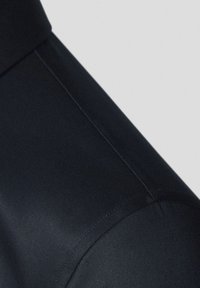 Zbliżenie na czarny materiał z gładką teksturą, wyraźnie zdefiniowanym kołnierzem i precyzyjnym przeszyciem, podkreślające elegancki wygląd.