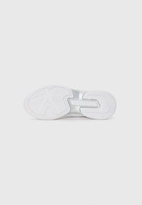 Suela de zapatilla deportiva blanca con goma texturizada para mayor agarre. Presenta un corte central y una marca en relieve. Superficie lisa sin patrones.