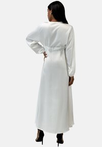 Lange mouwen witte satijnen jurk met een ceintuur in de taille, vloeiend ontwerp en subtiele glans. Gladde textuur en enkellengte met een rechte snit.