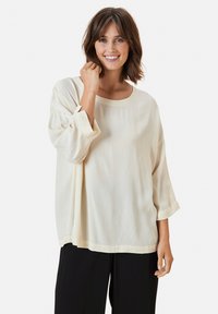 Blusa morbida color crema con collo rotondo e maniche a tre quarti. Realizzata in tessuto leggero con una texture liscia.