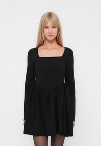 Vestido negro con escote cuadrado, mangas largas y una falda acampanada con detalles fruncidos en la cintura. Textura de tela suave.