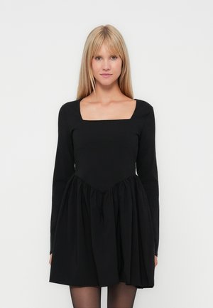 Robe noire au décolleté carré, manches longues, et jupe évasée avec des détails froncés à la taille. Texture de tissu lisse.