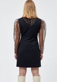 Schwarzes Nadelstreifenkleid mit einer taillierten Silhouette, durchsichtigen Leopardenmusterärmeln und einem V-Ausschnitt hinten. Glatter Stoff und strukturierte Form.