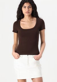 Bruin aangesloten t-shirt met een wijde ronde hals, gecombineerd met een witte denim rok. De stof is glad en rekbaar.
