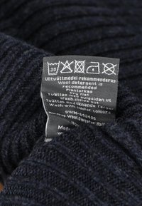 Navy blue knitted wool label with care instructions, showing washing symbols and recommendations for using wool detergent and drying flat.
